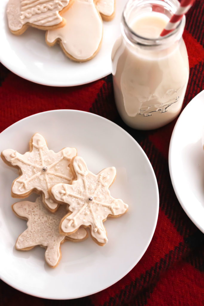 Sugar Cookies on a white round plate, on red plaid background with glass of milk.
