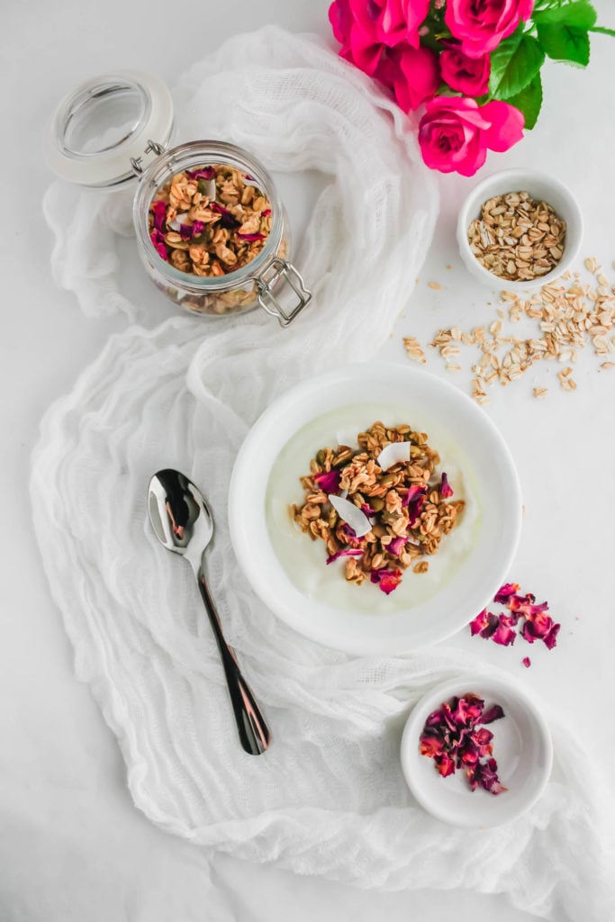 Rose Tahini Cardamom Granola in white bowl with spoon on the side.