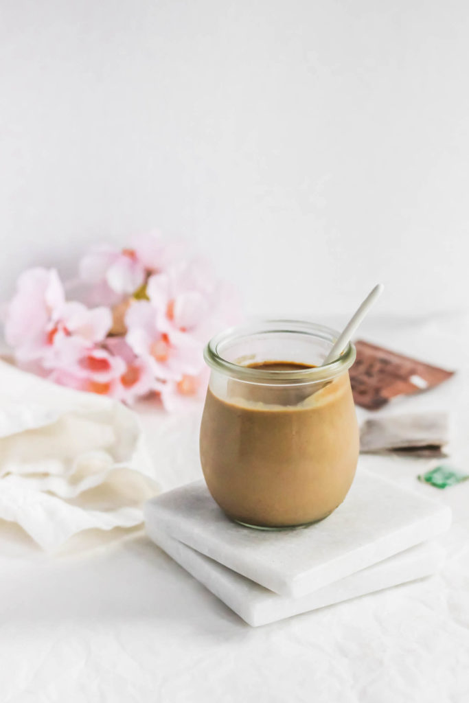 Jar of Hojicha Roasted Green Tea Milk Jam with spoon, on marble coasters.