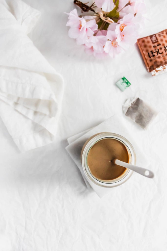 Jar of Hojicha Roasted Green Tea Milk Jam on white marble coaster, with tea bag and white linen.