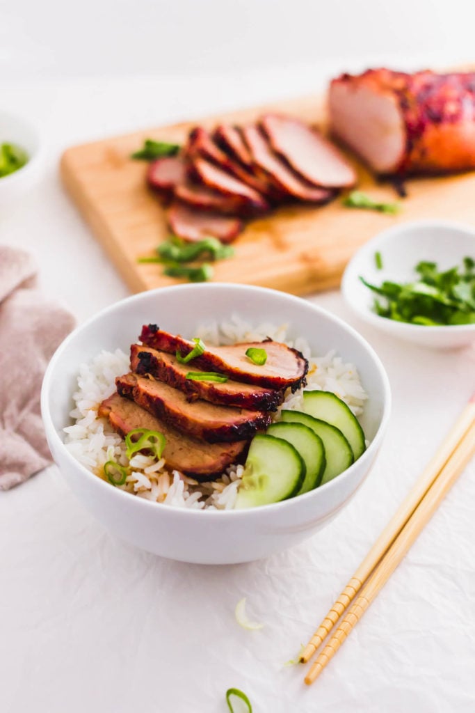 Roasted char siu bbq pork on top of rice in white bowl.