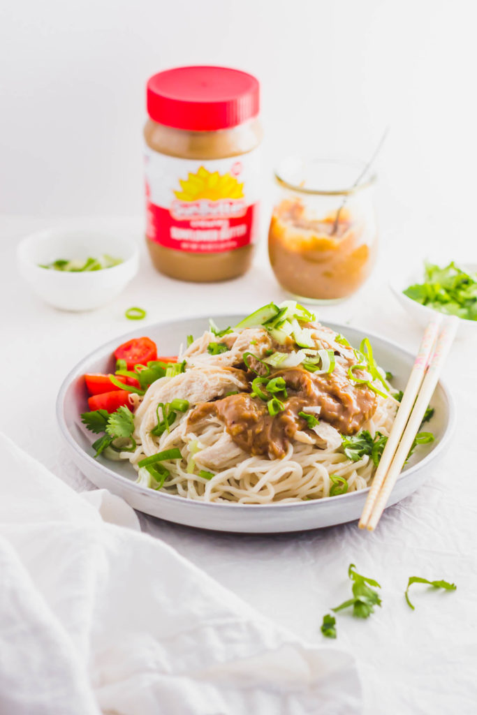 Sunbutter Chicken Noodles with Cucumber on round plate with chopsticks, SunButter jar in background.