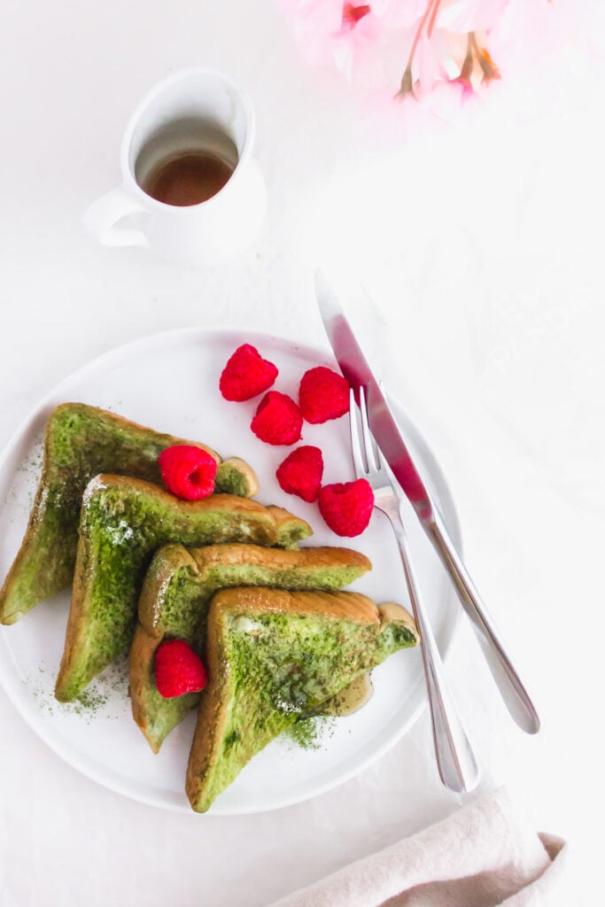 Close up of Pandan French Toast on round white plate with raspberries and fork.