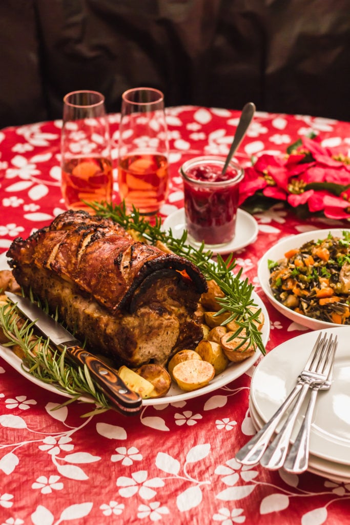 Holiday Roast Pork With Wild Rice Stuffing with plates, forks, glasses.
