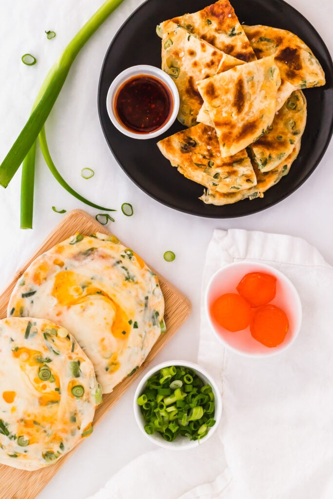 Salted egg yolk green onion pancakes on wooden board, cut up pancakes on black plate.