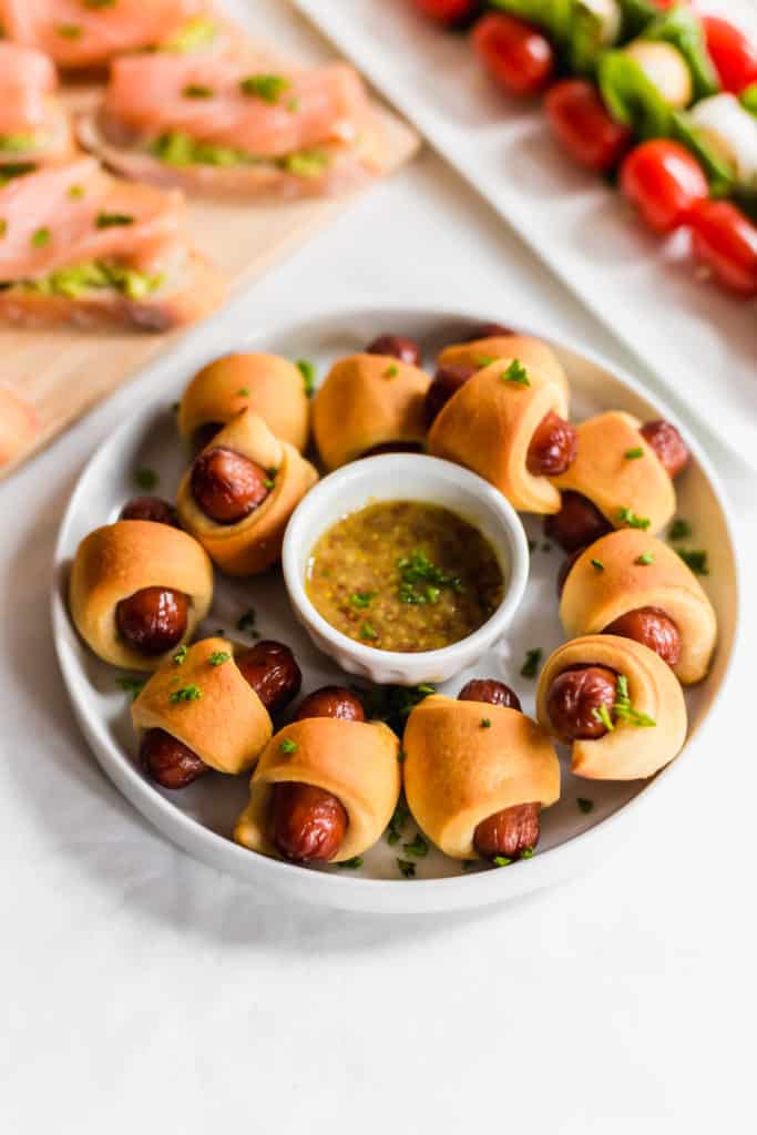 Close up of sausage rolls on white round plate with small sauce bowl in middle.