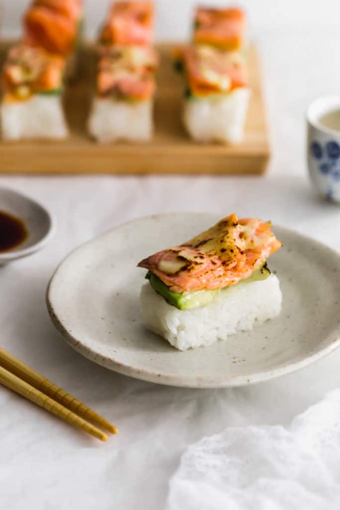 Aburi salmon sushi on beige plate with chopsticks on side.