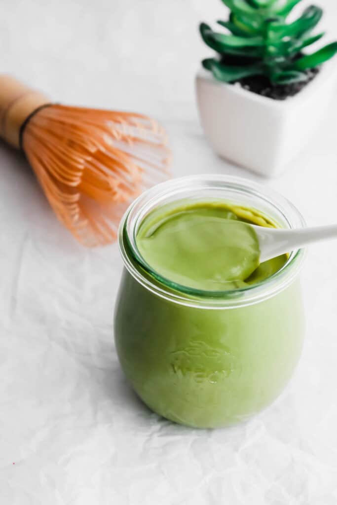 Spoon scooping Matcha Milk Green Tea Spread in jar.
