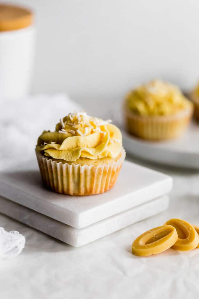 Close up of coconut cupcake and passionfruit frosting with coconut flakes, yellow chocolate callets in the foreground.