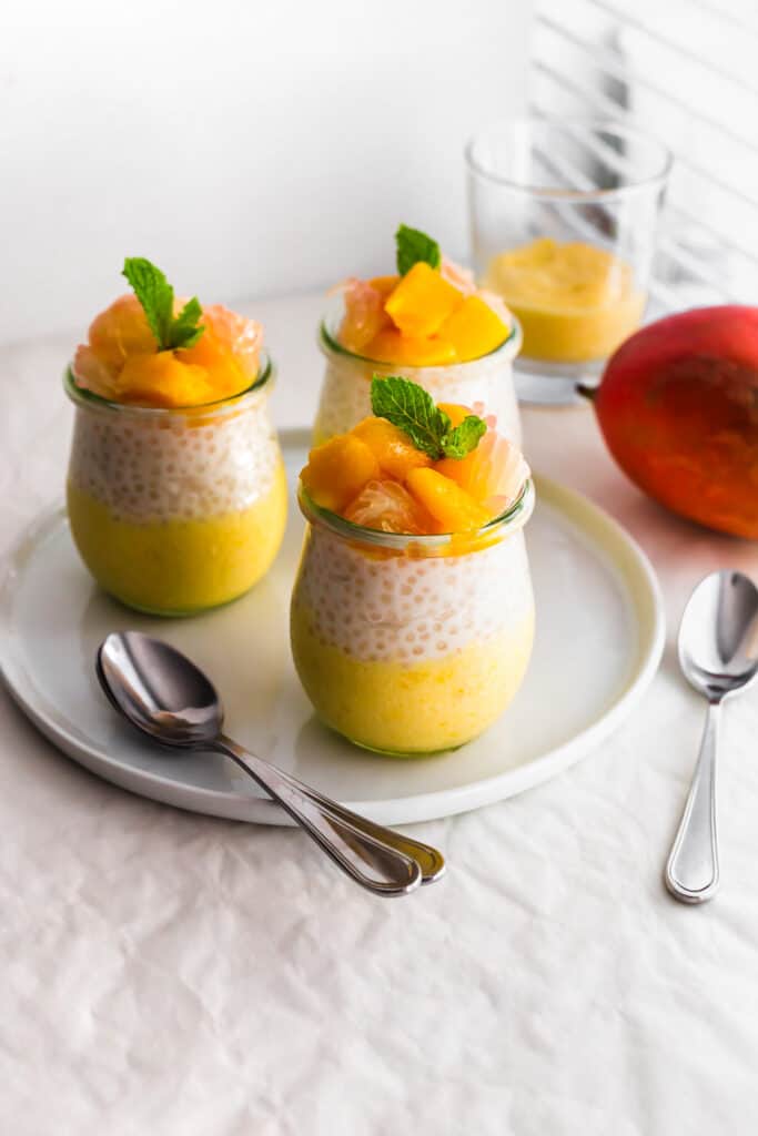 Jars of mango pomelo sago on white plate with spoons on the side.