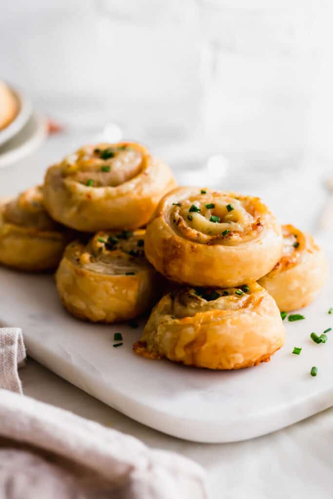 A stack of ham and cheese puff pastry scrolls topped with chives on marble.