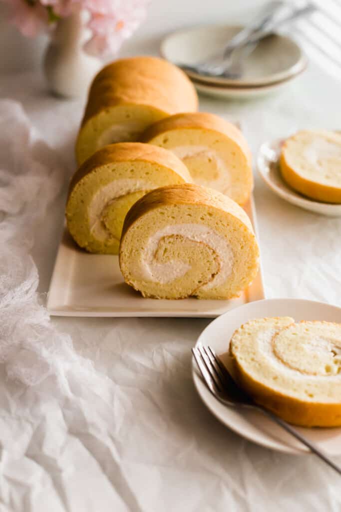 Close up of slices of yellow roll cake with white cream on rectangular plate.