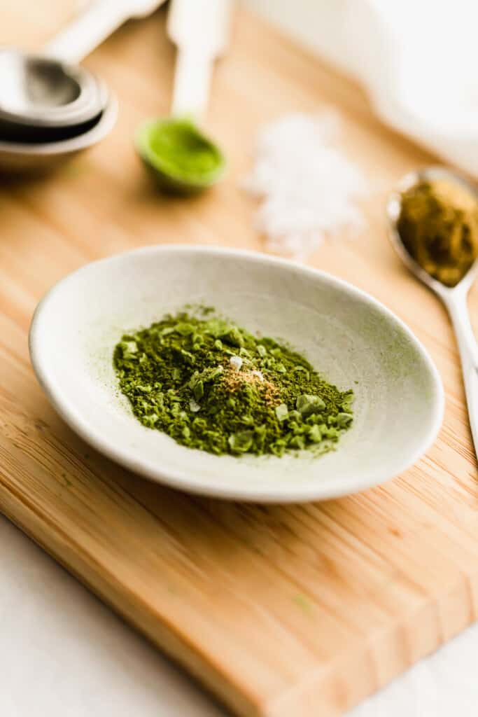 Close up of matcha cumin salt in a dish on wooden board.