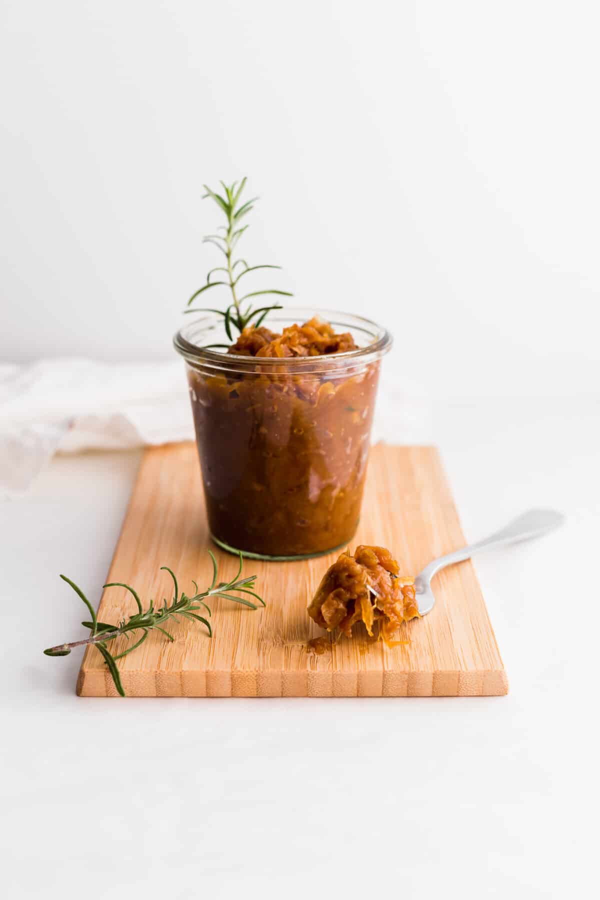 Fork full of onion jam on wooden board with jar in the background.