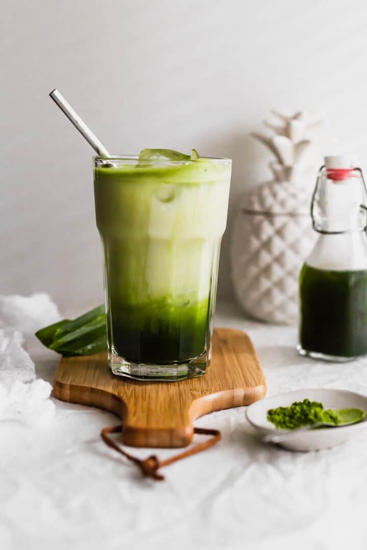 Glass of matcha latte with stainless steel straw on wooden paddle.