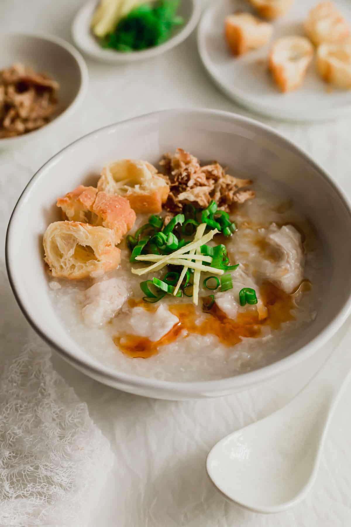 Chicken congee in a white bowl with various toppings.