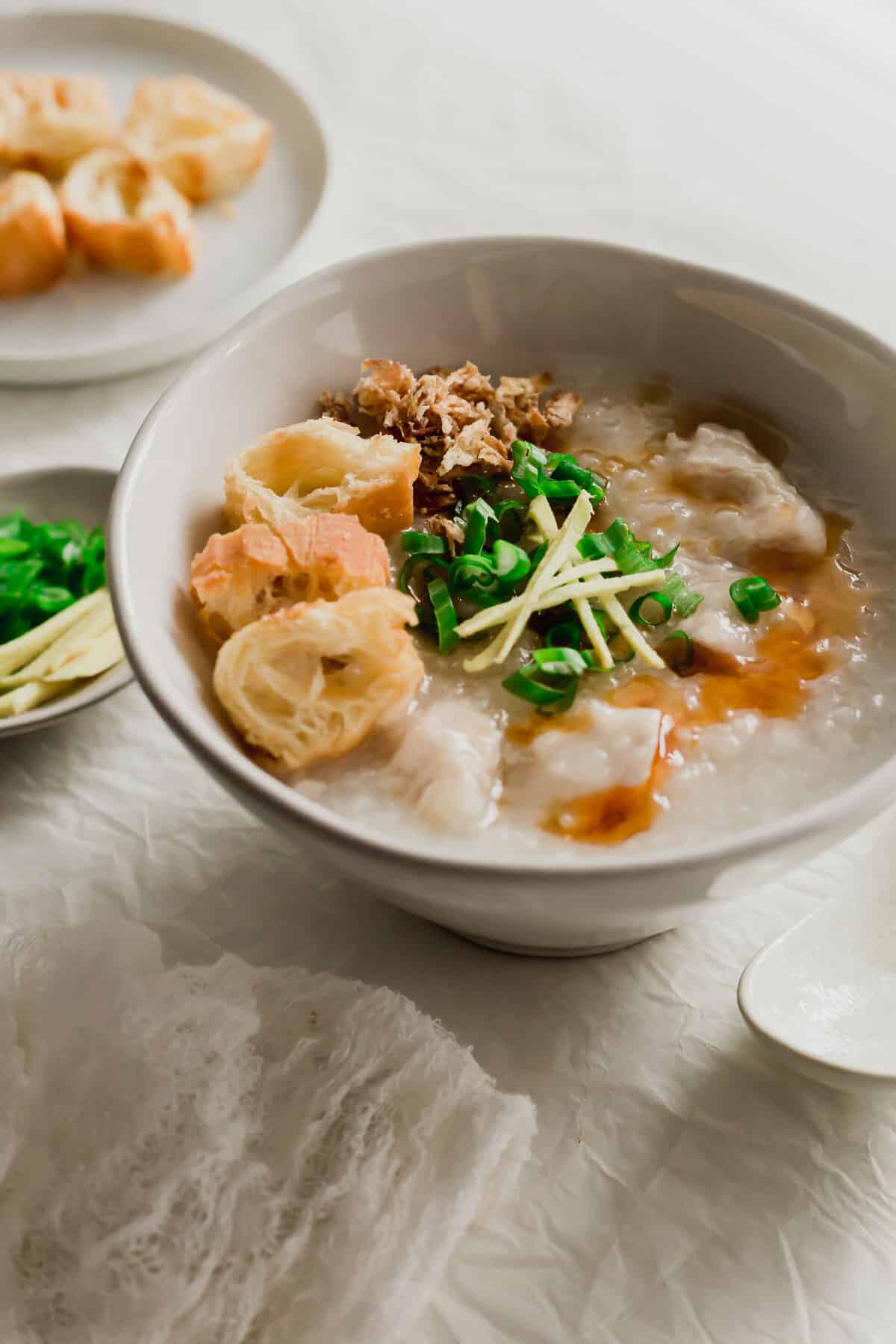 Chicken congee in a white bowl with various toppings.