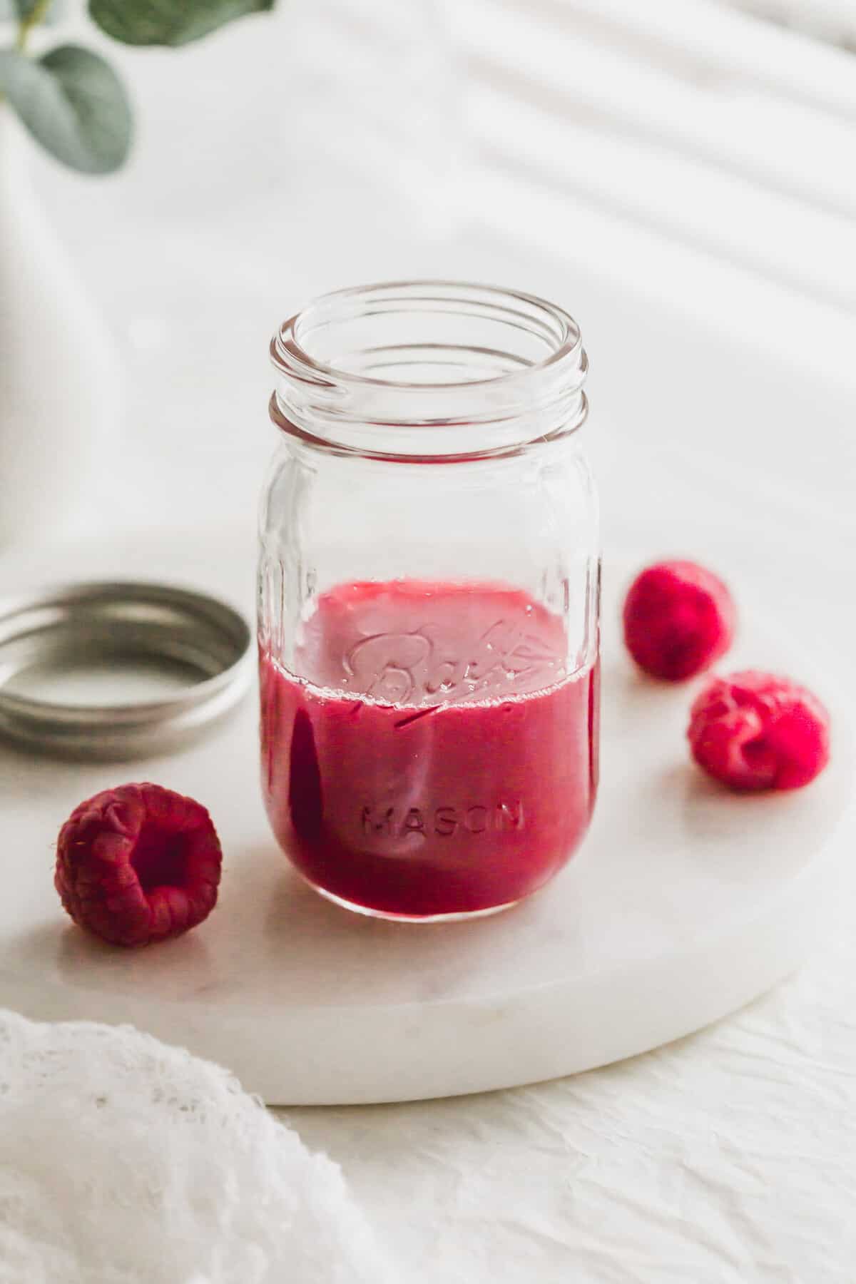A glass half filled with raspberry syrup.
