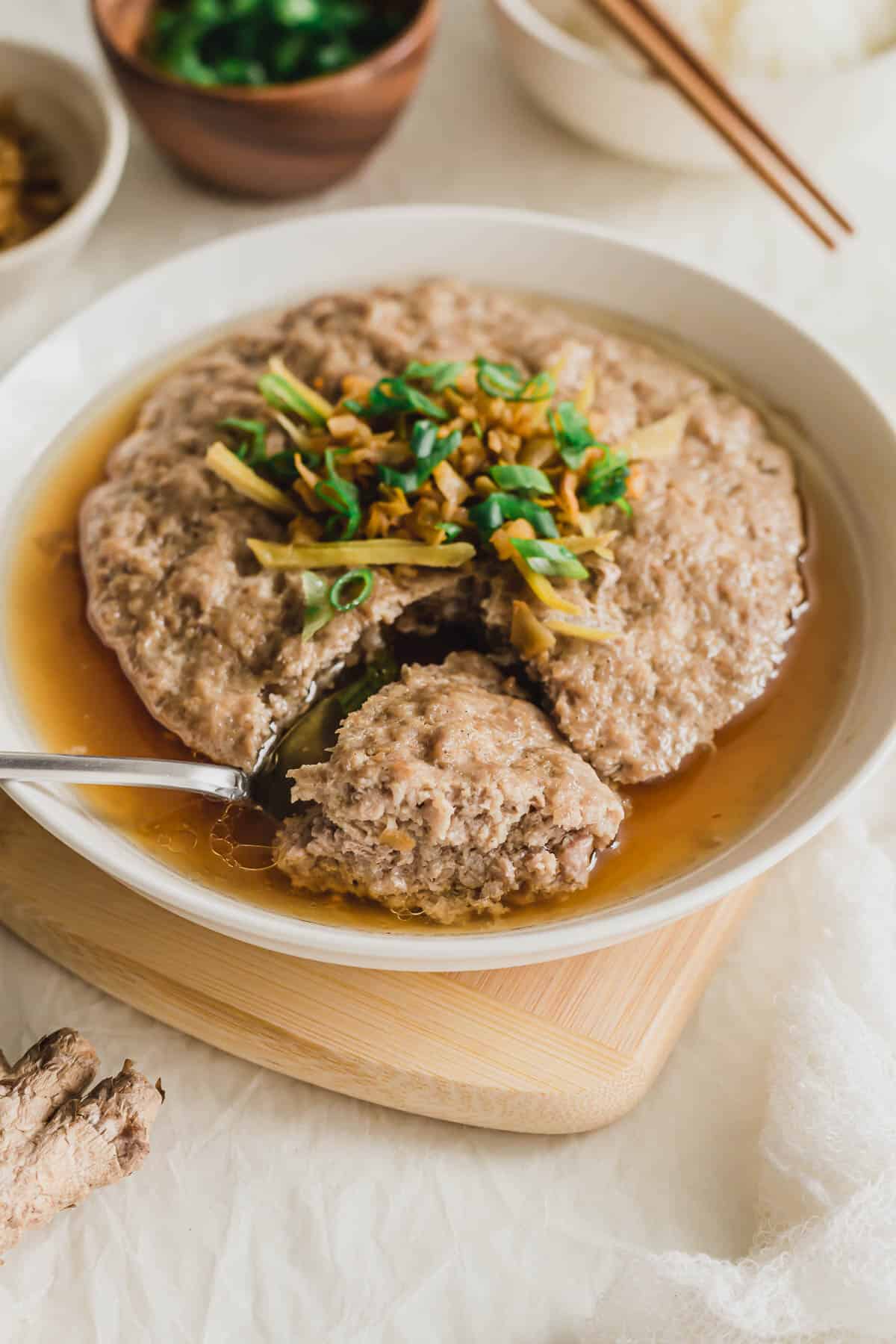 A spoonful of Chinese steamed pork patty in a white plate on wooden board.