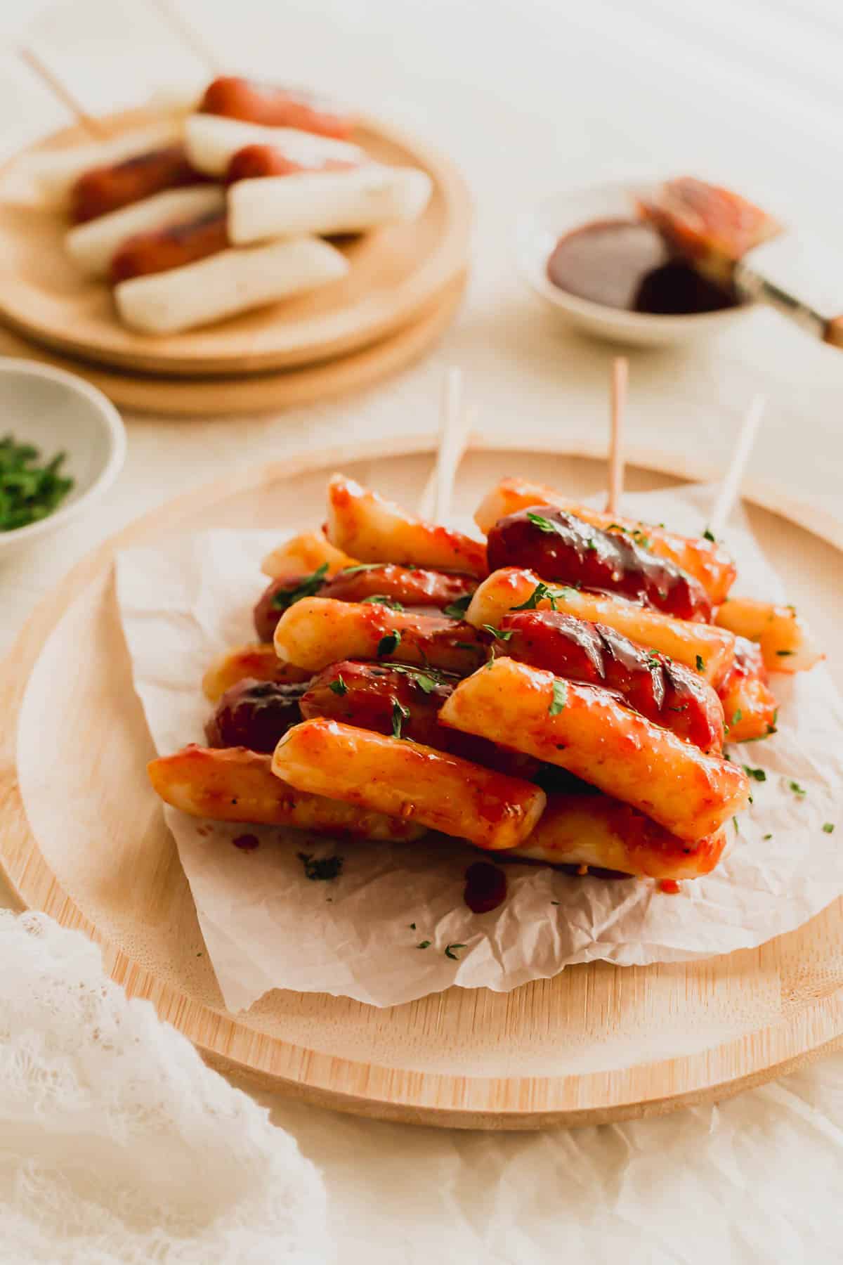 Sotteok Korean skewered rice cakes and sausages on a piece of white parchment paper on wooden round plate.