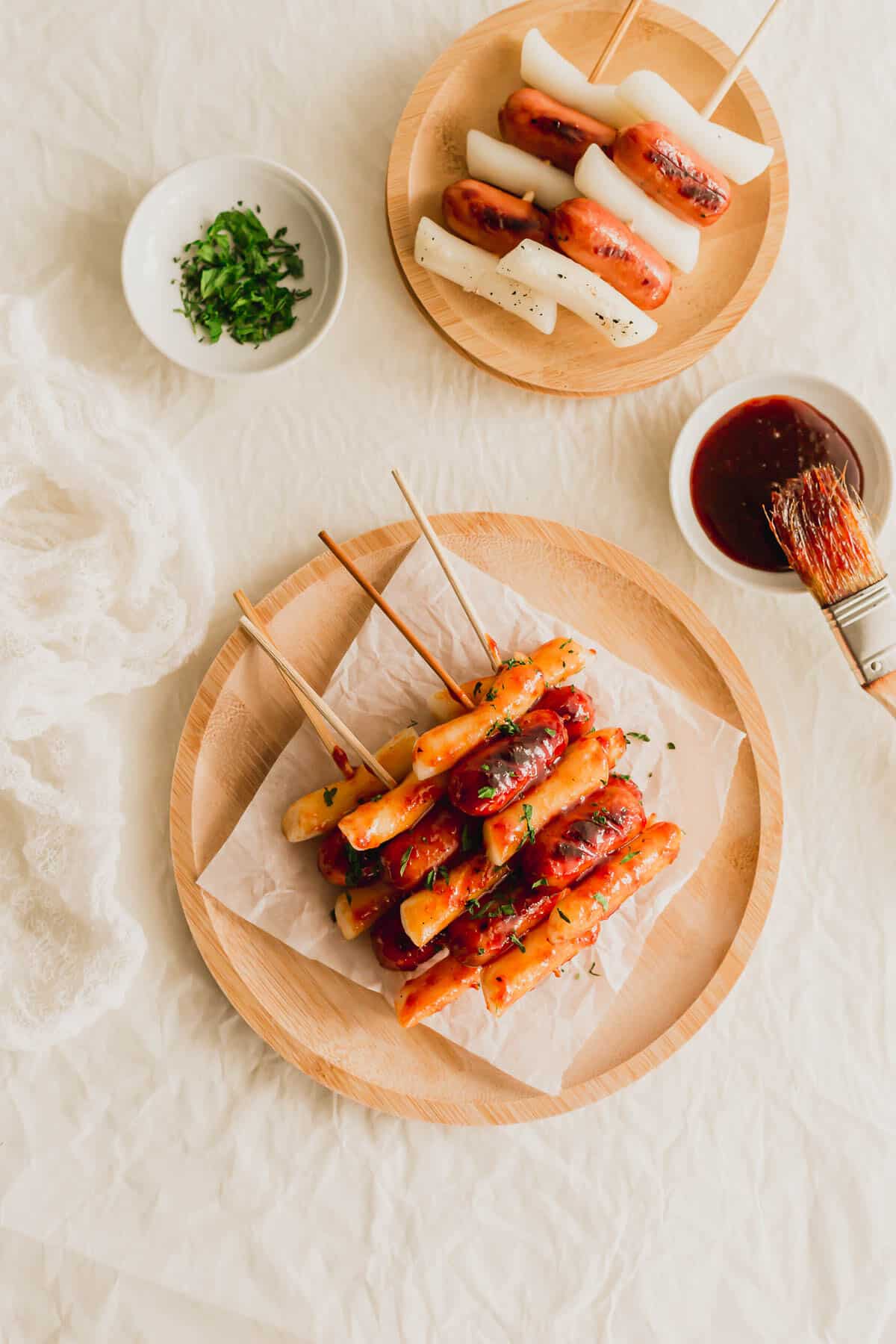 Korean Sotteok skewered rice cakes and sausages on a piece of white parchment paper on wooden round plate.
