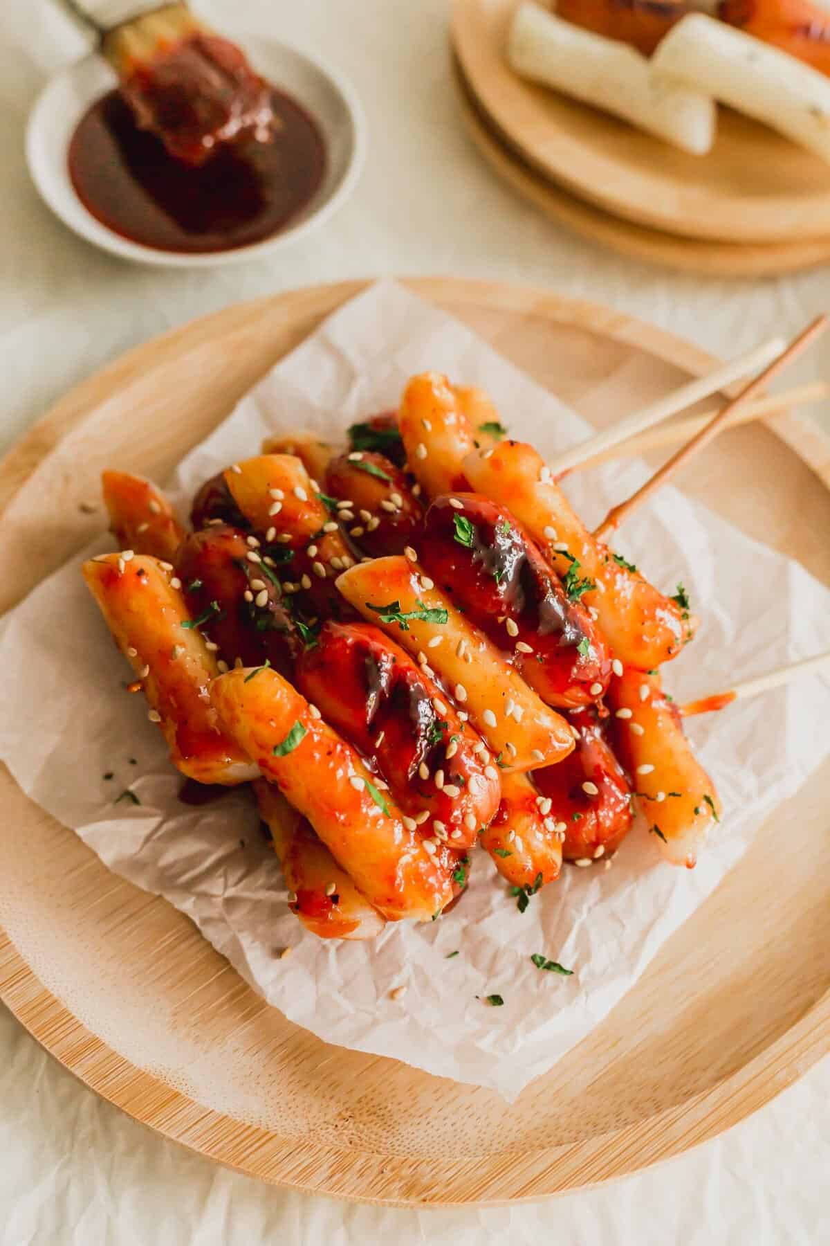 So-tteok skewered rice cakes and sausages on a piece of white parchment paper on wooden round plate.