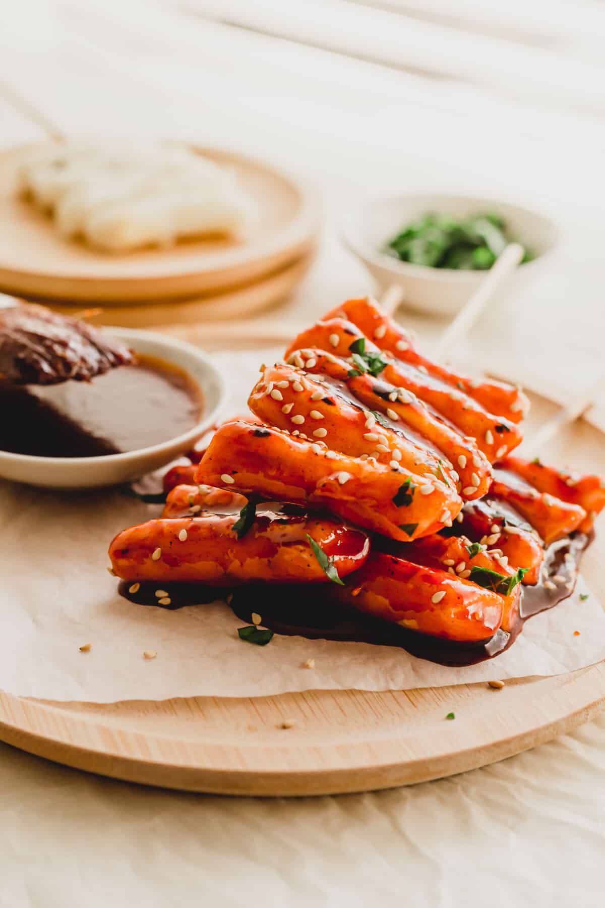 Skewered Korean rice cakes tteokkkochi on a piece of parchment paper on wooden round plate.
