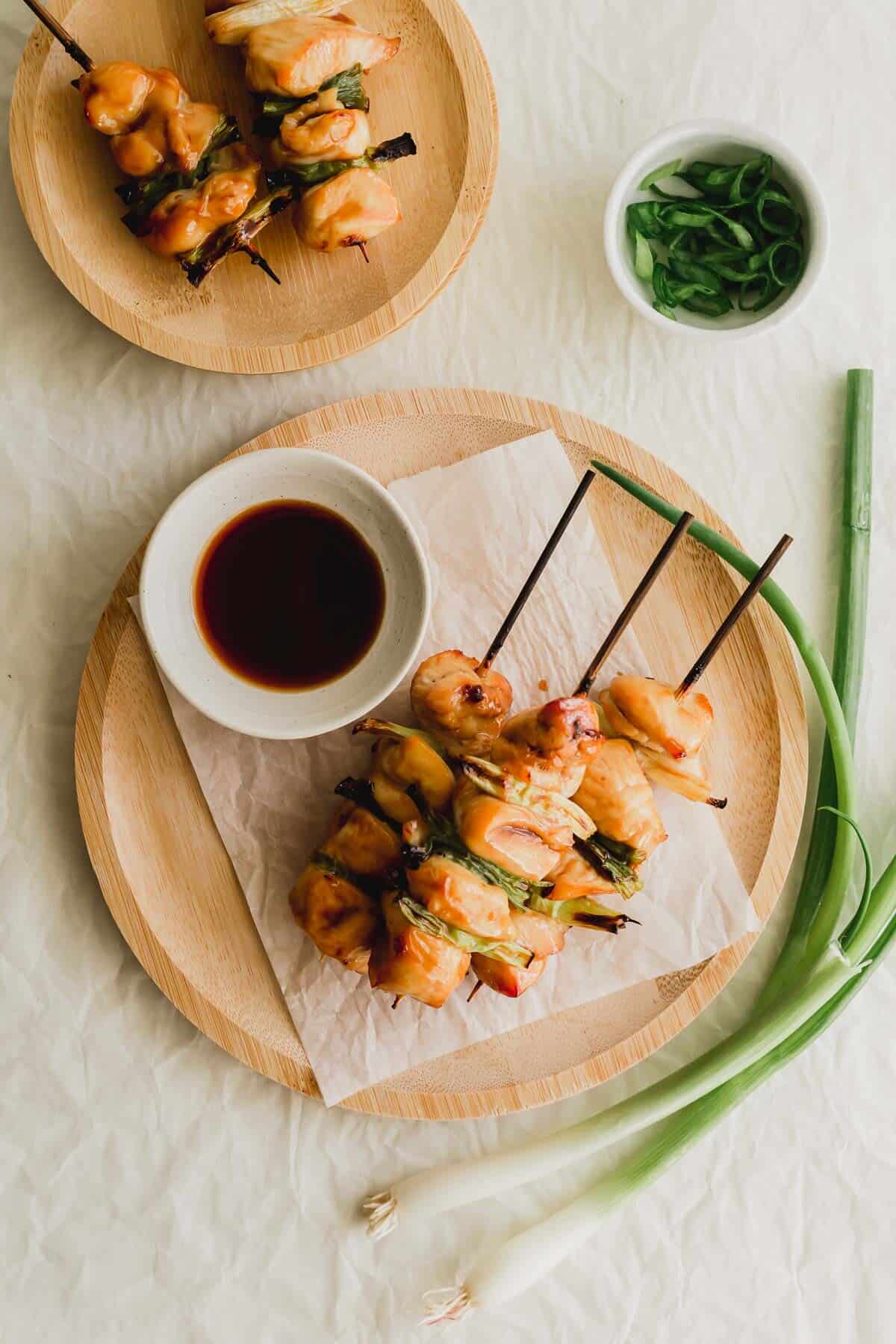 Grilled chicken yakitori skewers on a white parchment paper on wooden plate.