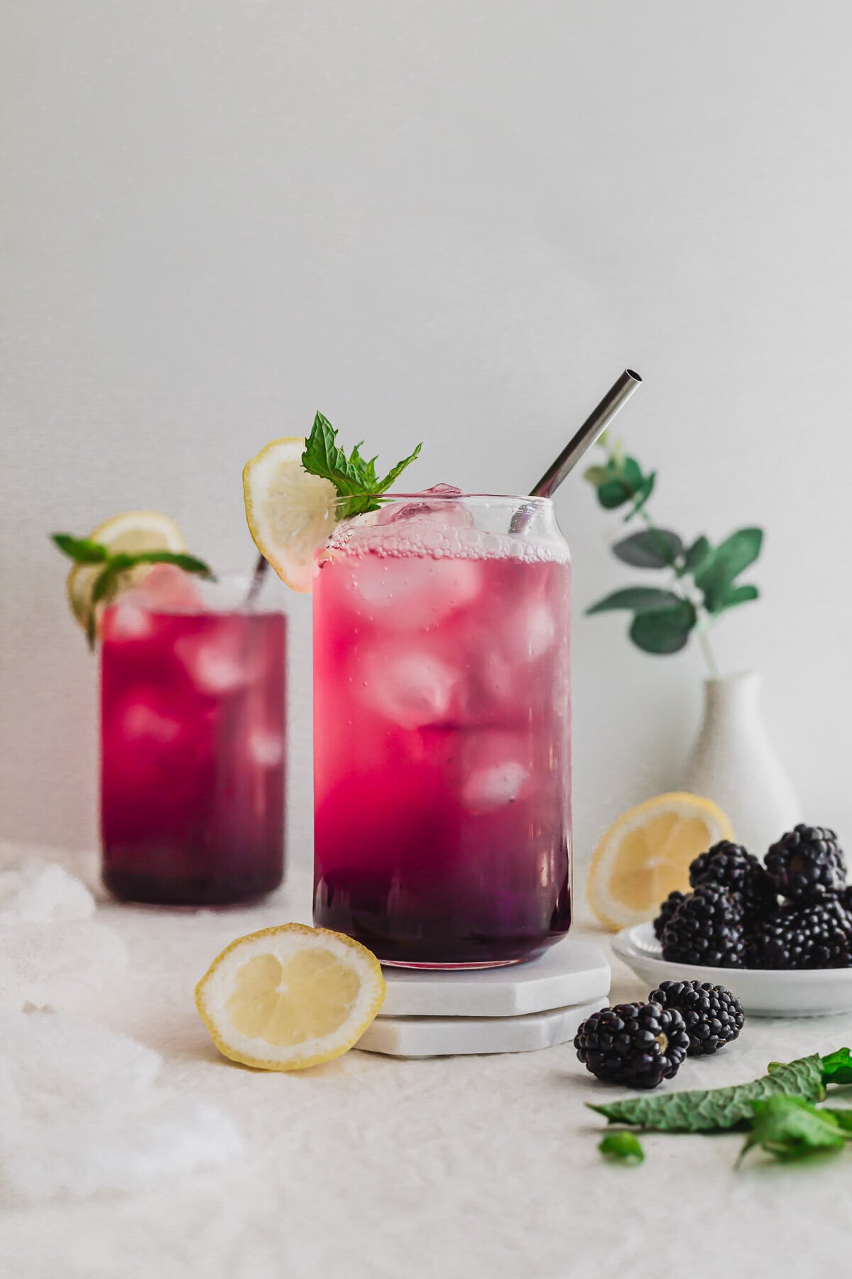 Sparkling blackberry yuzu drink in a glass with straw on stacked white coasters.