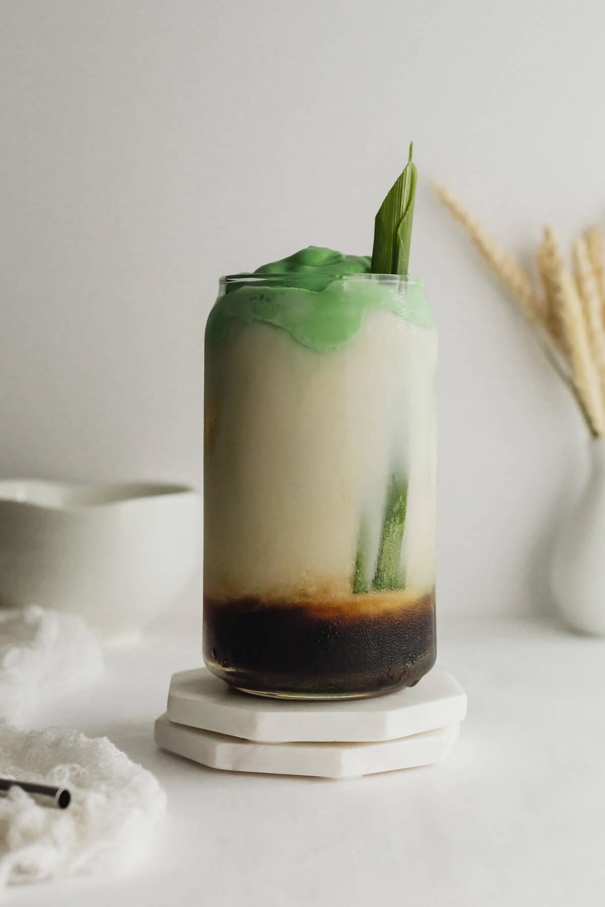 Pandan latte in a glass on white marble coasters.