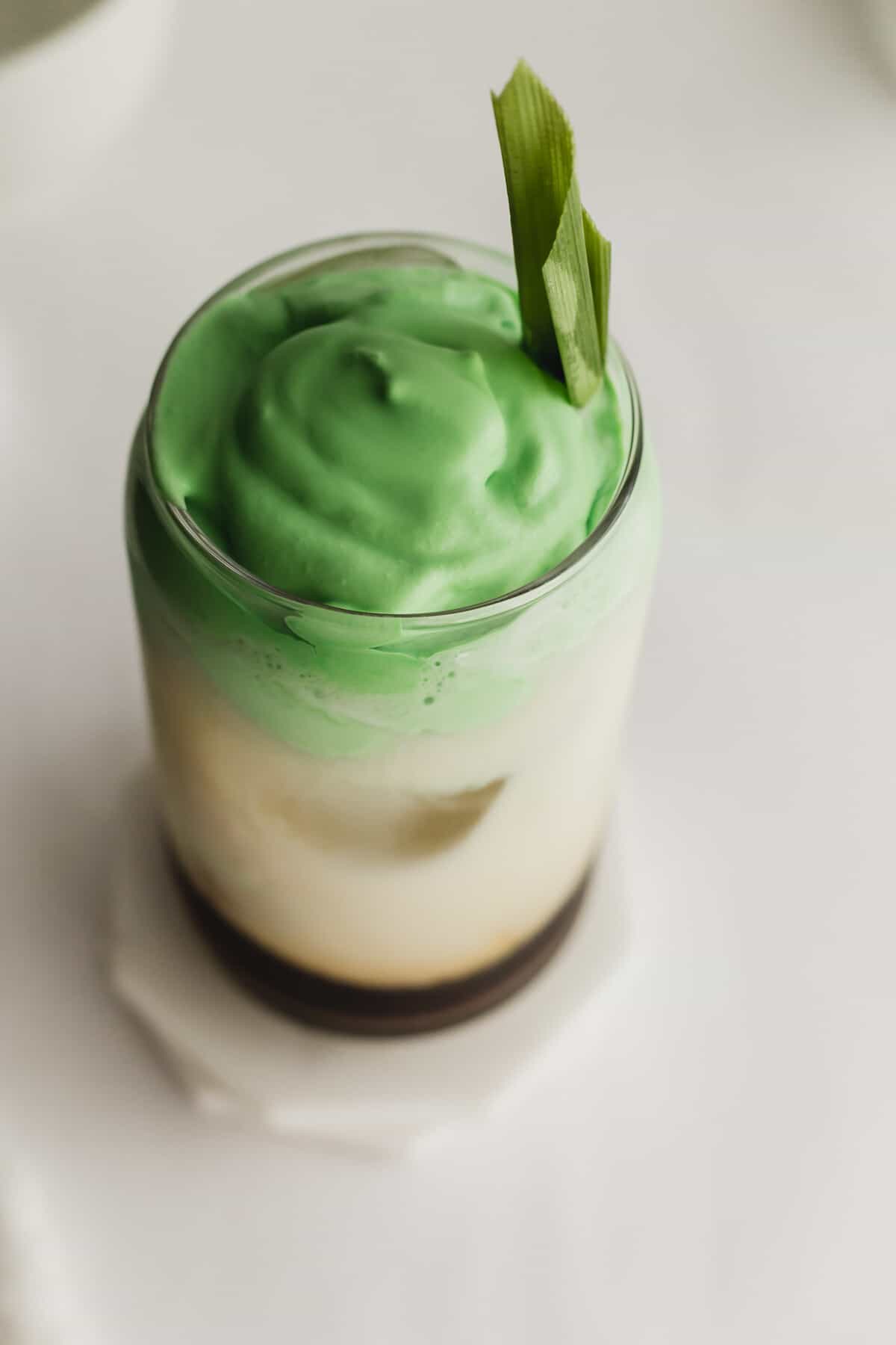 Pandan latte in a glass on white marble coasters.