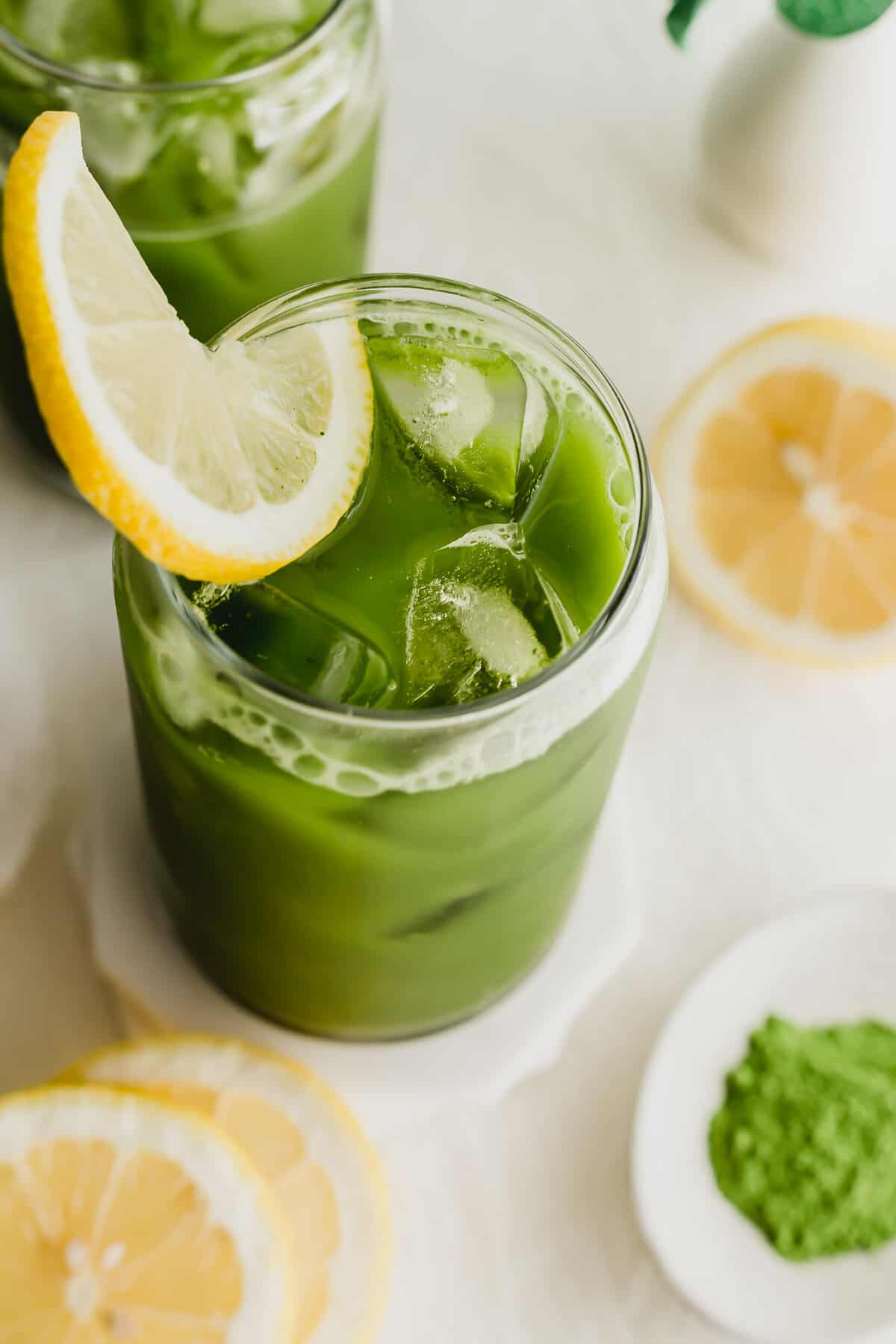 Close up of glasses of matcha tea lemonade with lemon on white coaster.
