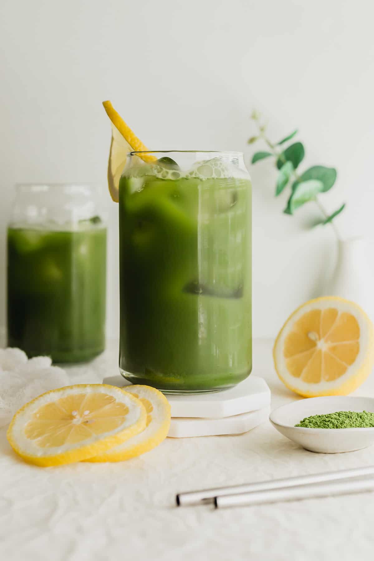 Glasses of matcha tea lemonade on white coaster.