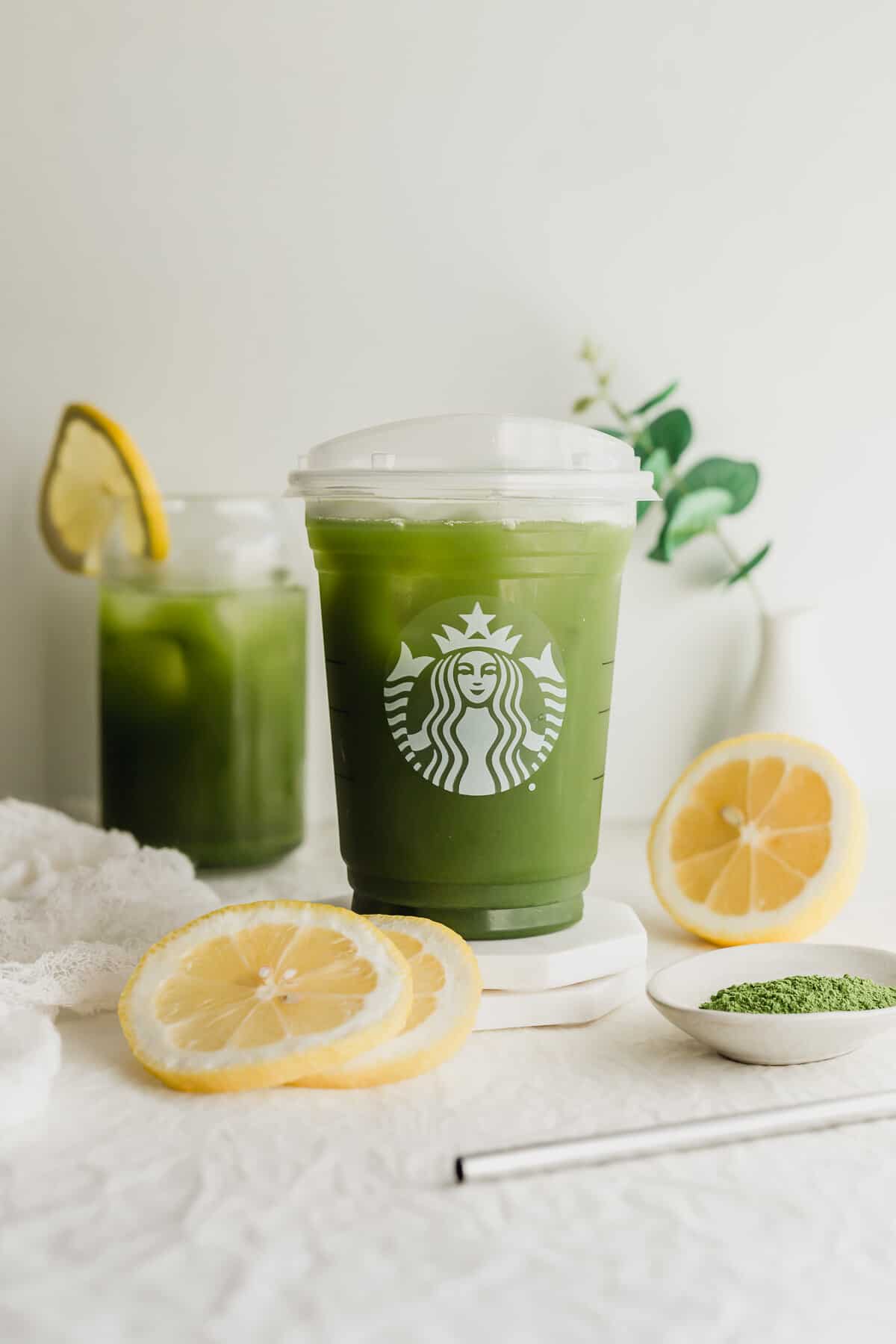 Matcha tea lemonade in Starbucks cup on white coaster, with sliced lemons on the side.
