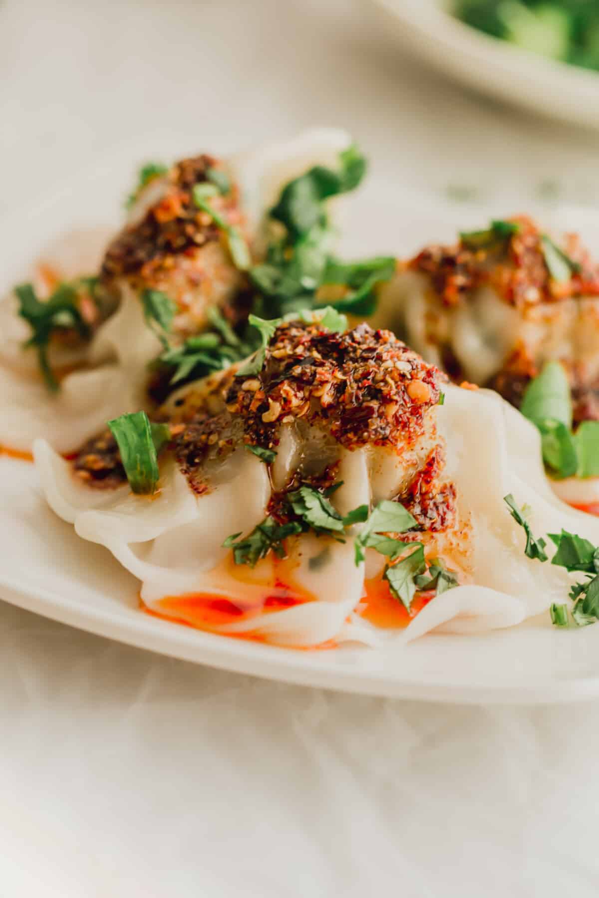 Close up of dumplings enrobed in chili oil on a white plate.