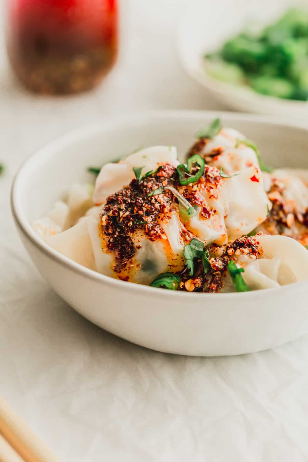 Close up of a white ceramic bowl with wonton dumplings drizzled with chili oil.
