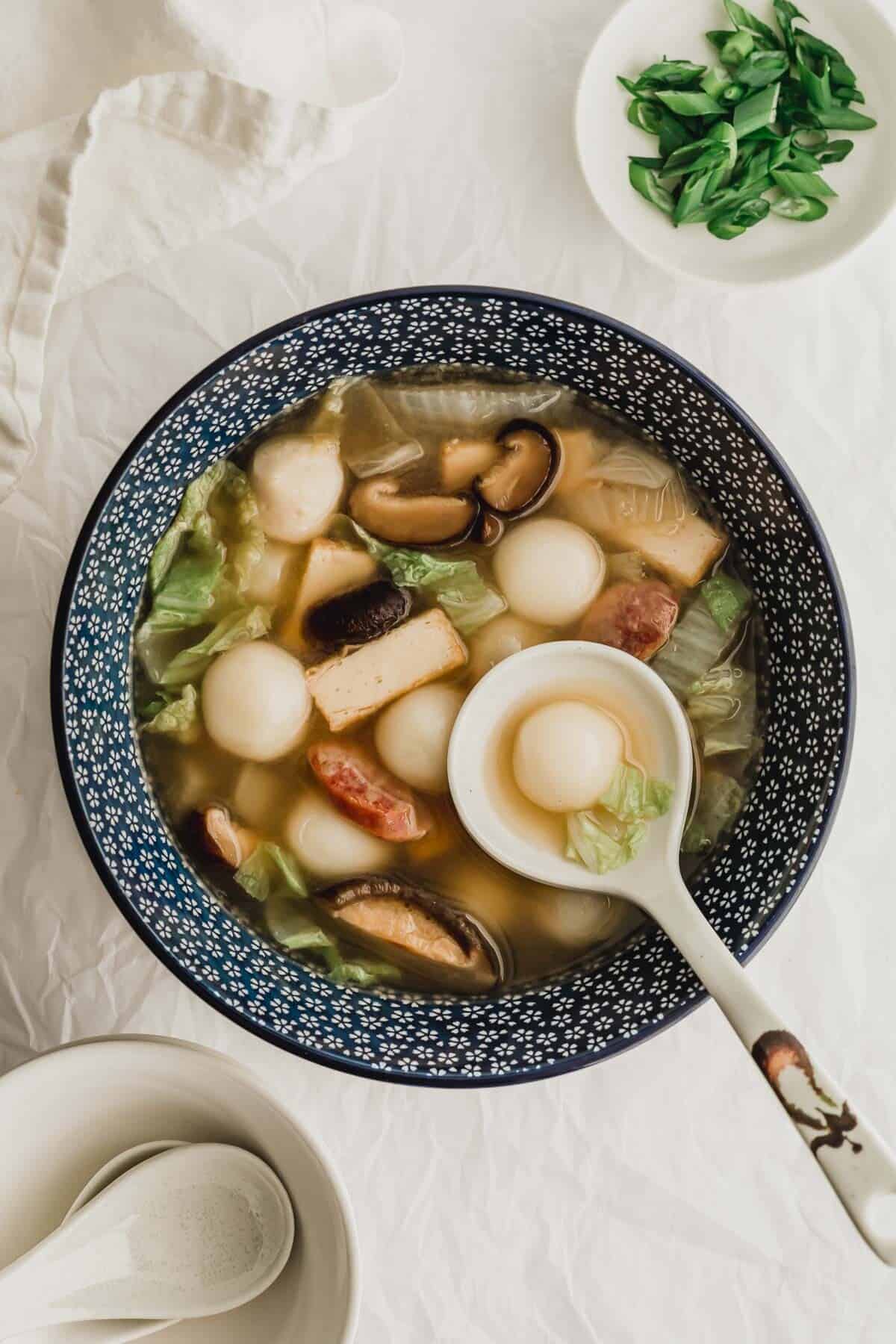 Savory tang yuan soup in a blue bowl with ladle.