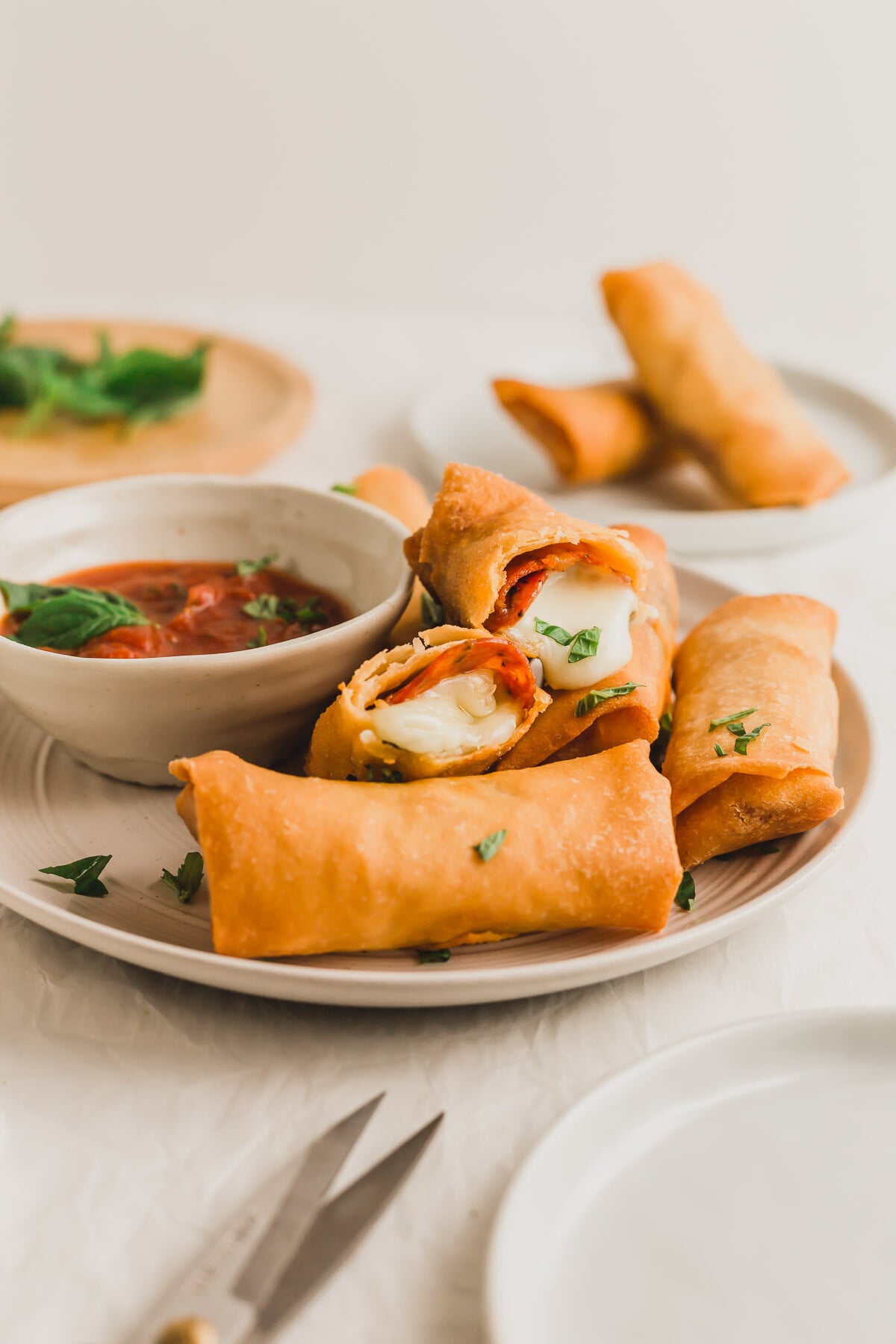 Pizza egg rolls on a plate, with tomato marinara sauce on the side.