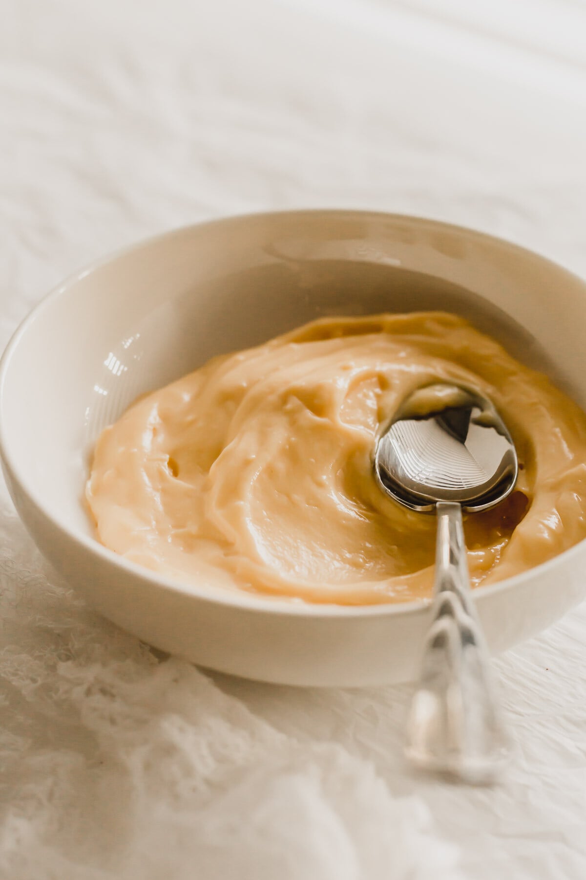 Vanilla pastry cream in a white bowl, with metal spoon.