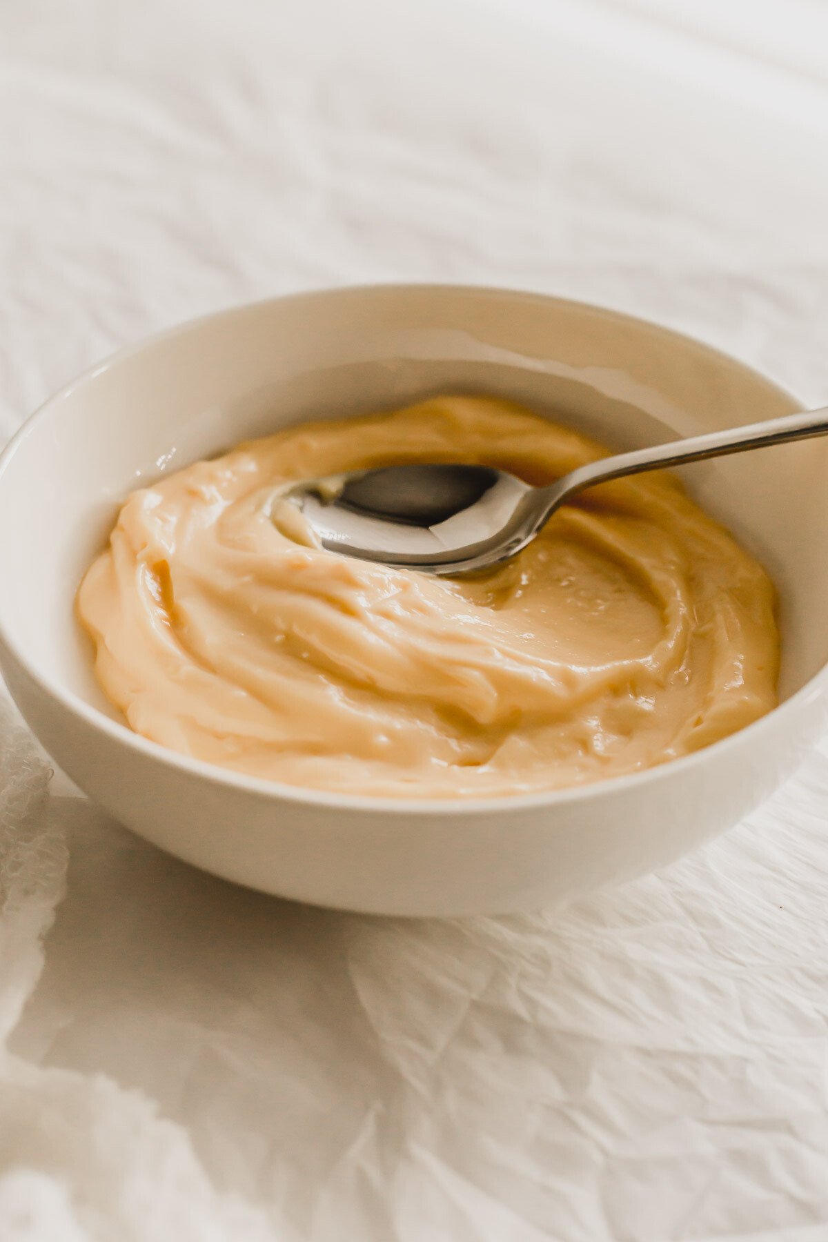 Vanilla pastry cream in a white bowl, with a spoon.