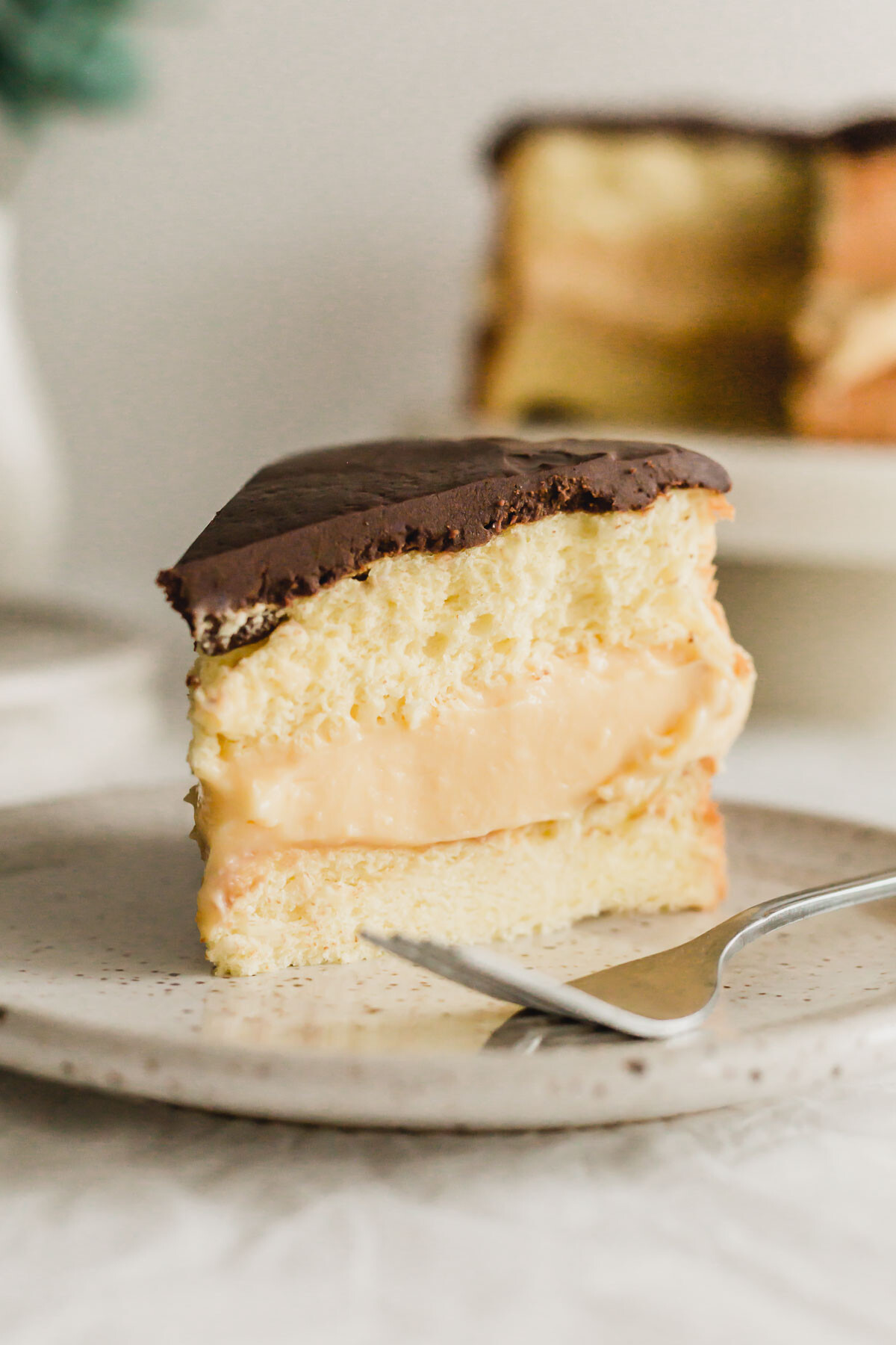 Slice of Boston cream pie on speckled plate, with fork.