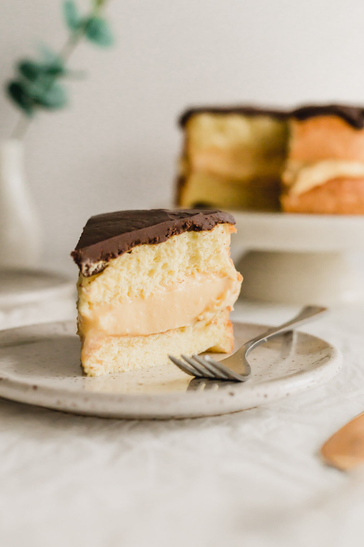 A slice of Boston cream pie on a speckled plate with fork.