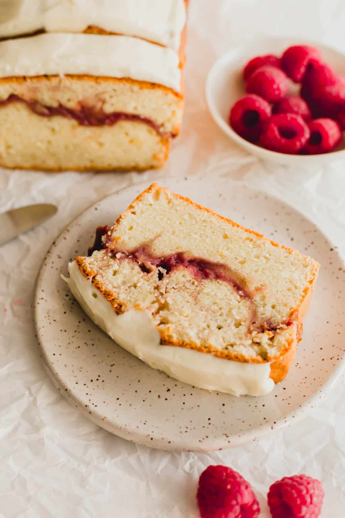 Slice of raspberry lemon loaf cake on a beige speckled round plate.