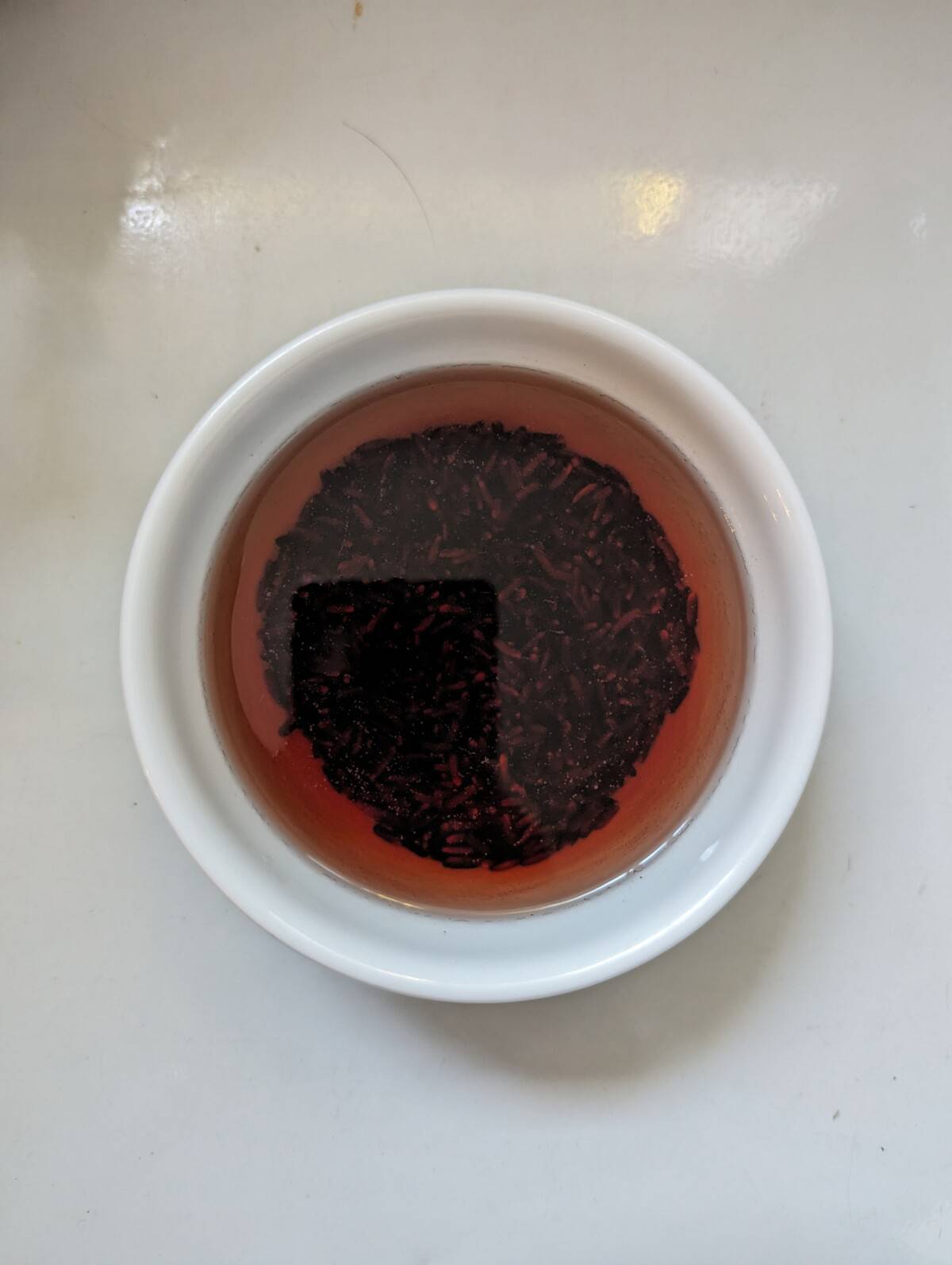 Black glutinous rice covered with water in a white bowl.