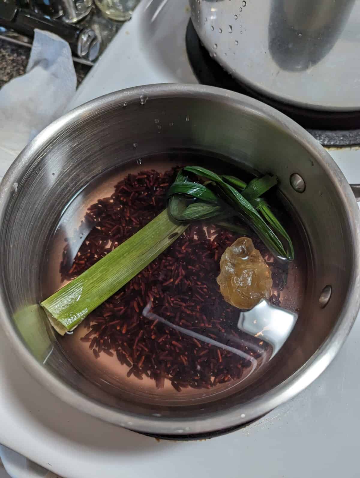 Metal saucepan filled with black glutinous rice, pandan leaf, sugar and water.