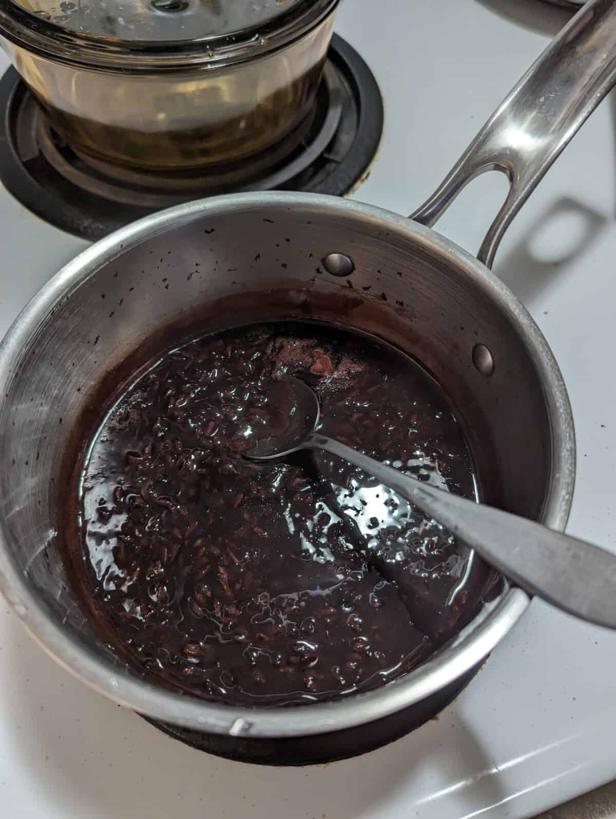 Pulut hitam in a metal saucepan with spoon.