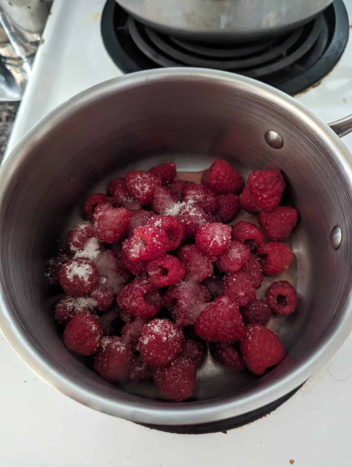Raspberries and sugar in a metal saucepan.
