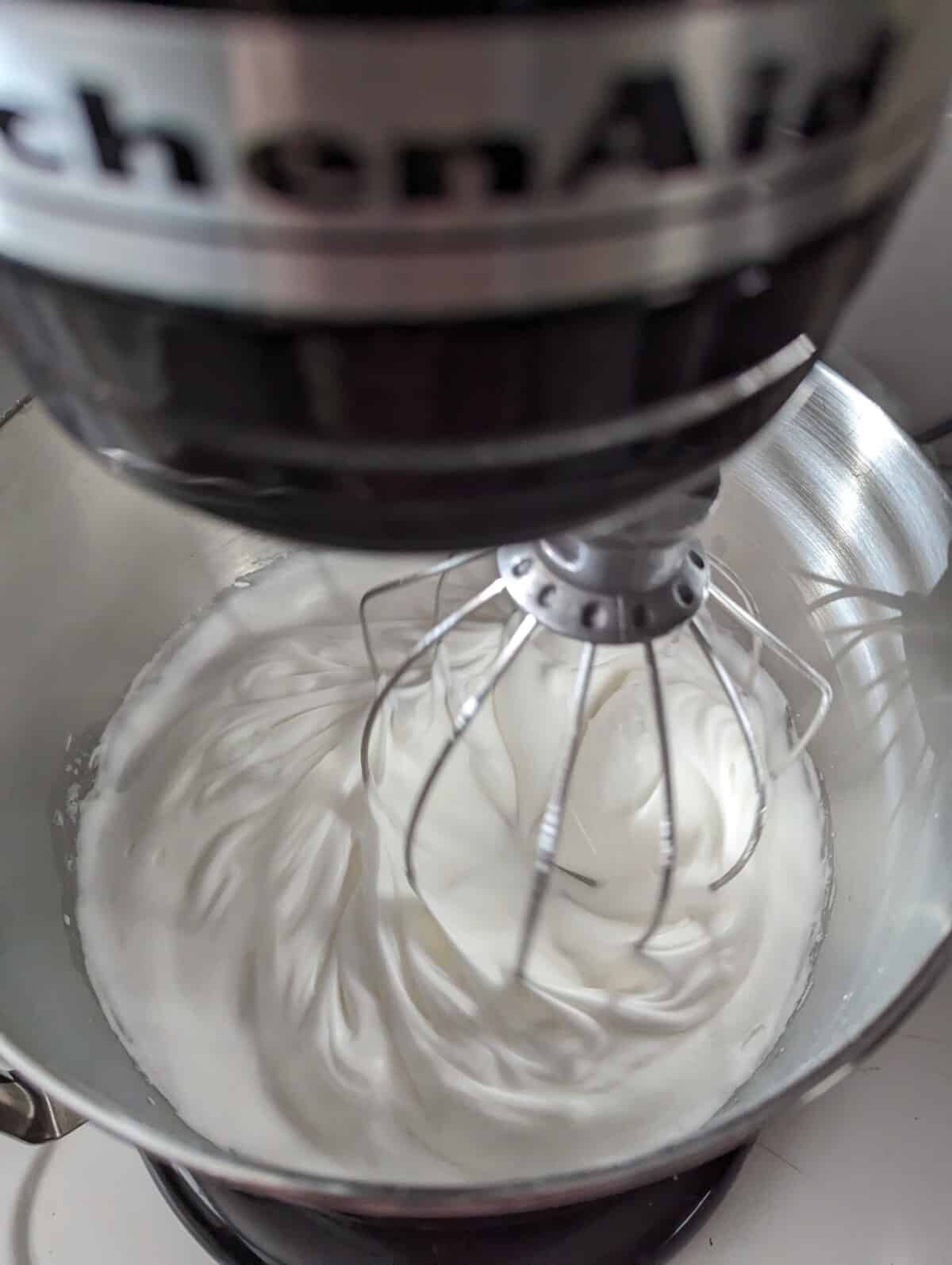 Whipped meringue in a stand mixer bowl with wire whisk.