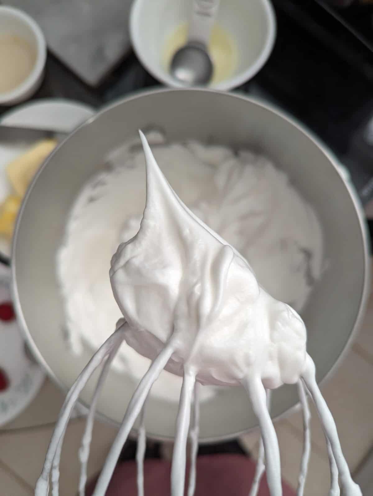 Egg white meringue on a wire whisk with a stiff peak pointing up.