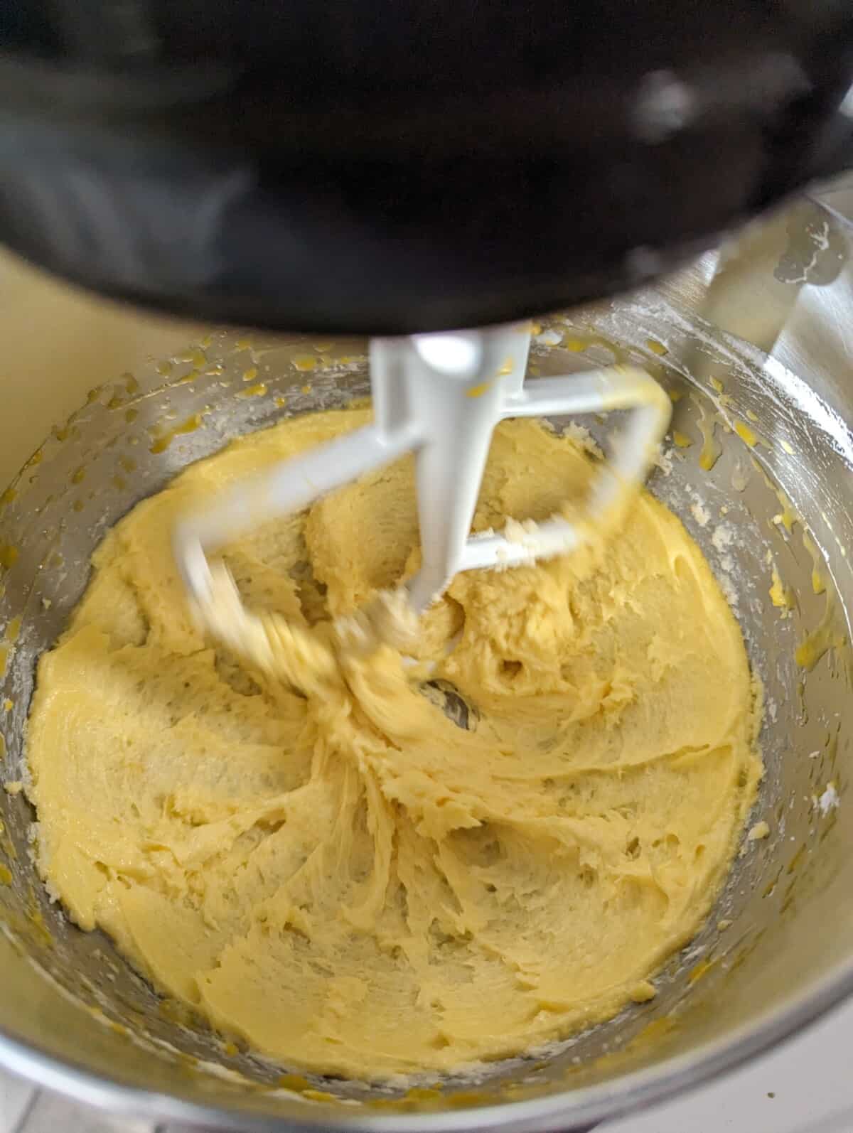 Yellow creamed butter in a metal stand mixer bowl with flat beater attachment.
